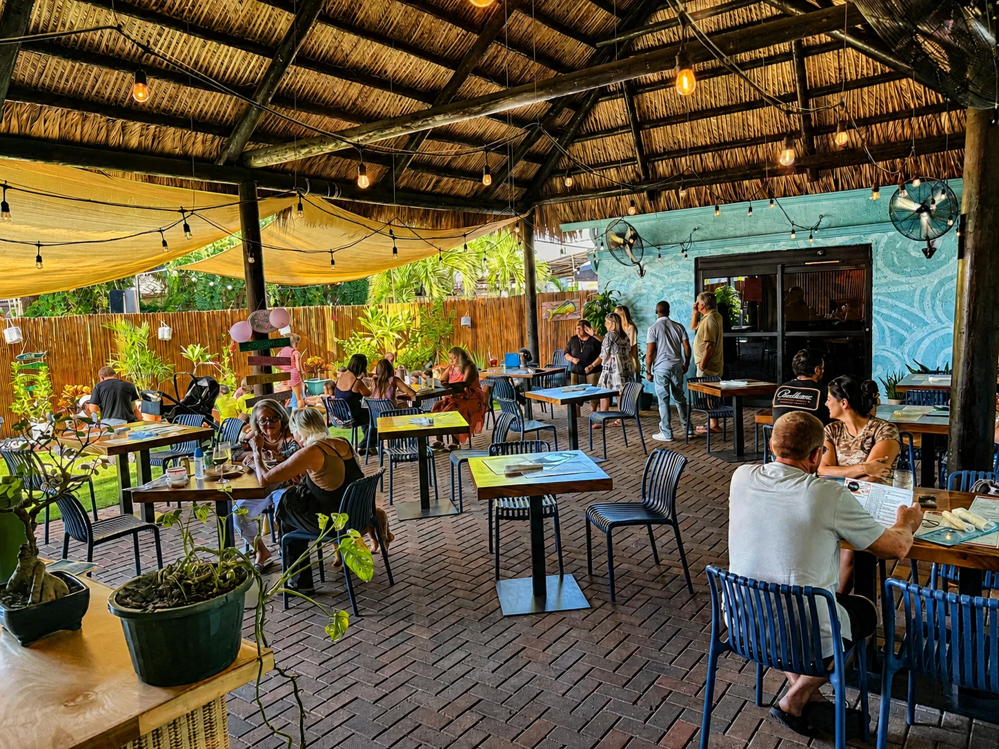 Guests dining on the covered tiki patio at The Catch, with string lights and a teal mural wall