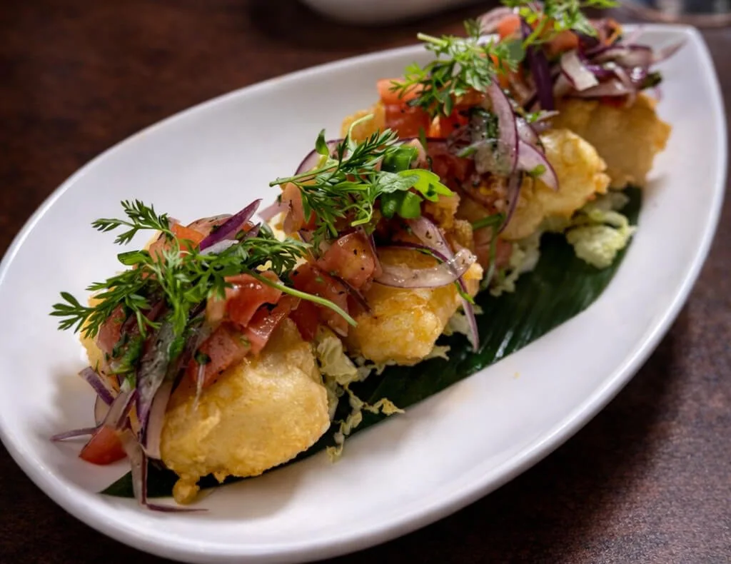 Close view of golden fried bites topped with red onion, tomato and herbs